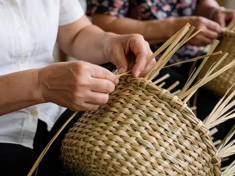 Adult hands weaving a straw basket with natural texture, soft lighting, earth tones, and artisanal detail