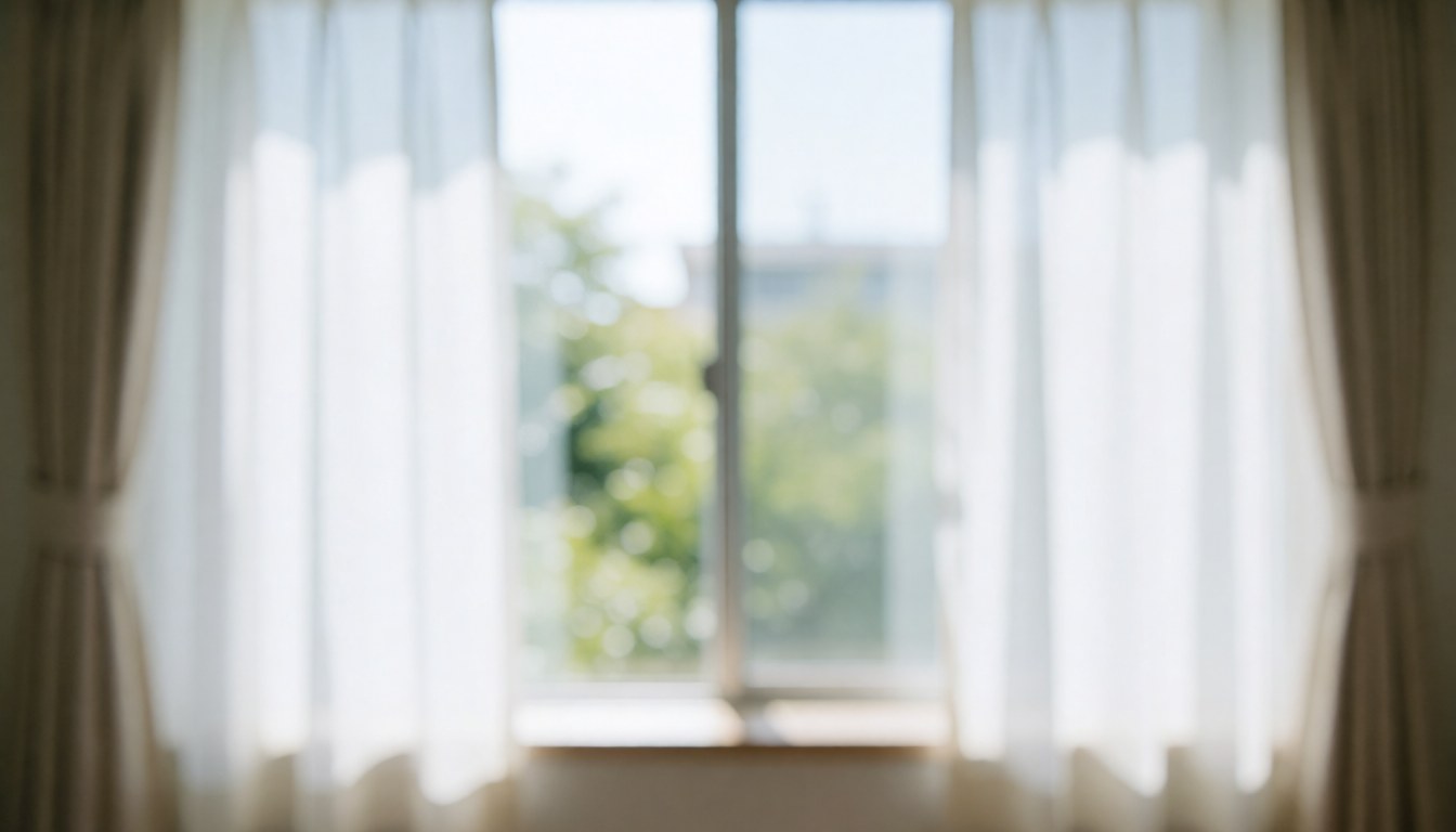A window with white curtains letting in soft natural light with trees visible in the background