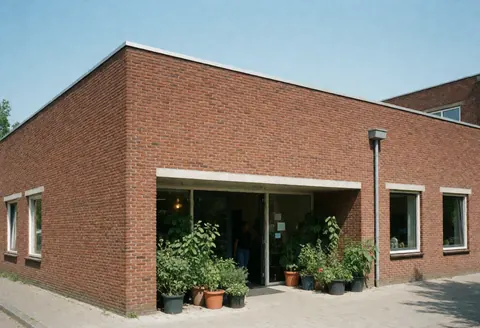 Modern red brick community building with wide entrance and potted plants under clear blue sky