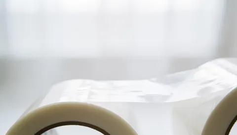 A roll of transparent packing tape placed on a soft white surface, suitable for moving company text overlays