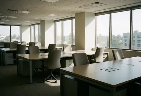 Spacious modern office interior featuring desks, chairs, and large windows letting in bright morning sunlight