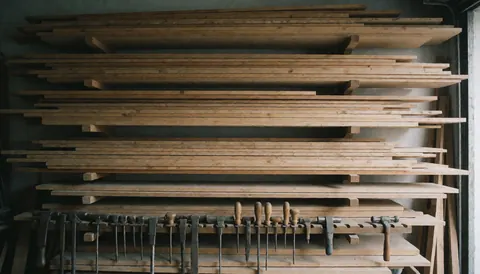 Stacks of wooden planks in a carpentry workshop with hanging tools, serving as a text background.