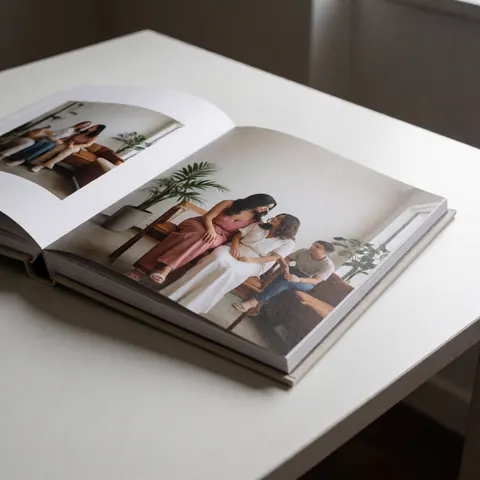 Open photo album on a white table displaying indoor portraits with high-quality paper and soft lighting