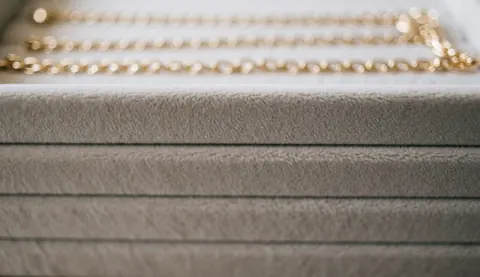 Blurred gold chains on a soft beige velvet texture, serving as an elegant background for jewelry store text and web design.