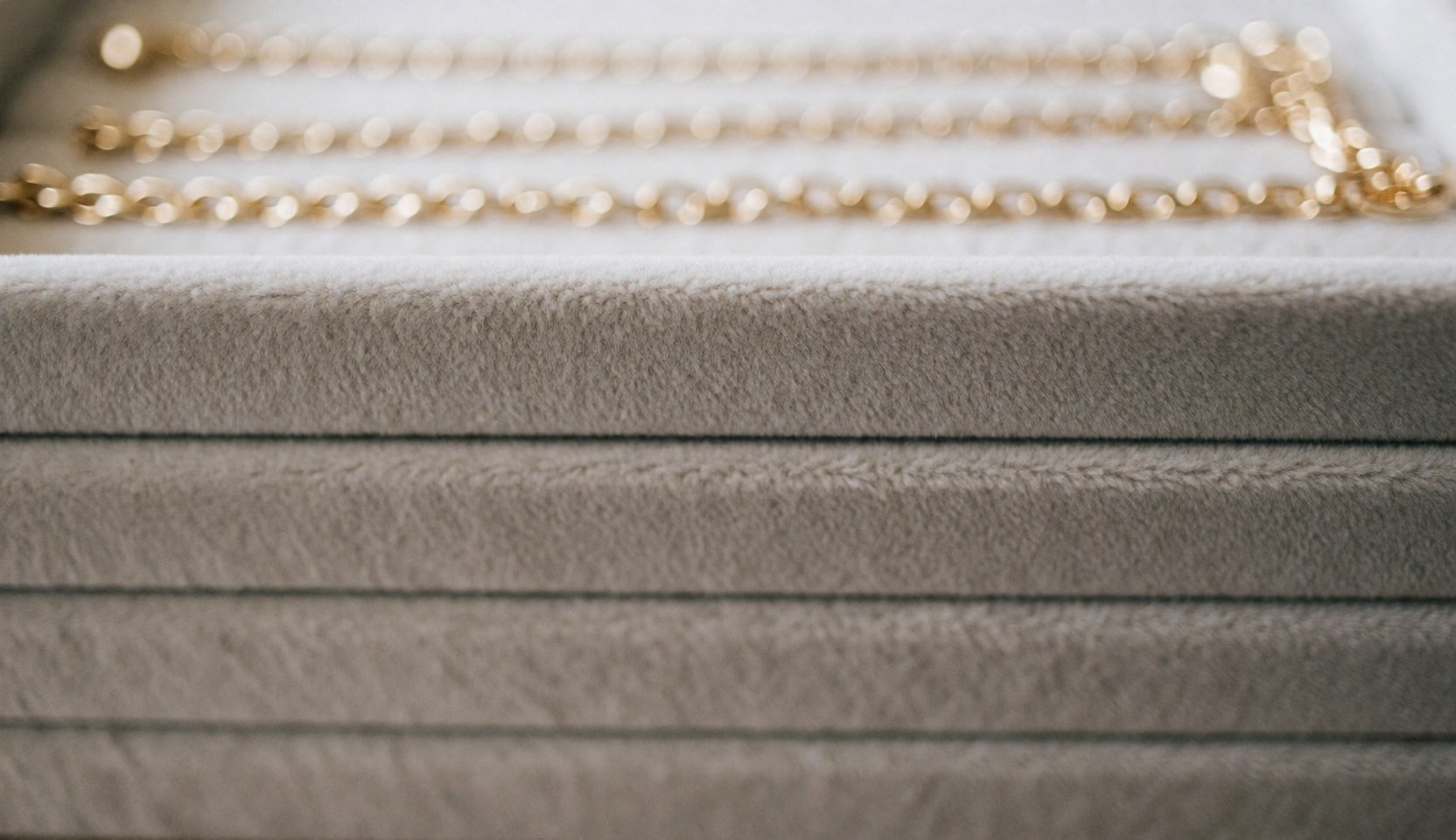 Blurred gold chains on a soft beige velvet texture, serving as an elegant background for jewelry store text and web design.