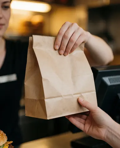A cashier hands a takeout food bag to a customer at the counter in a fast food restaurant.