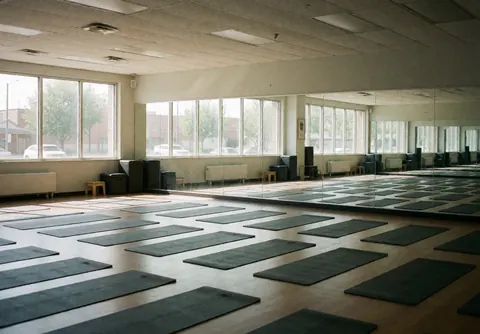 Empty yoga studio interior featuring neatly folded blankets, mirrors, and windows with natural light creating a calm atmosphere
