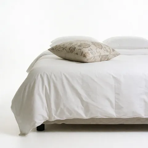 Close-up view of a hotel bed featuring crisp white sheets and a single floral patterned decorative pillow for hospitality marketing.