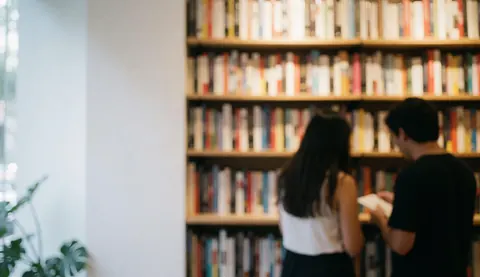 Background of bookstore shelves filled with books and two people browsing, warm minimalist atmosphere for text