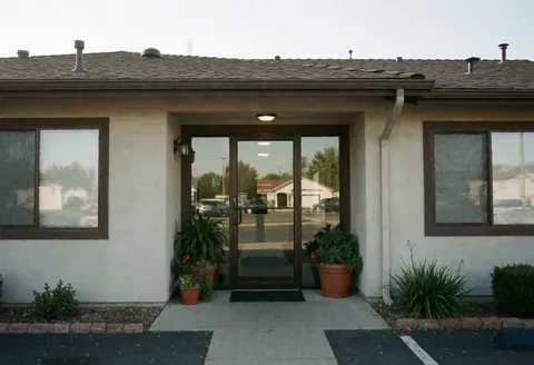 Professional office entrance featuring a glass door, potted plants, and clear sky creating a welcoming atmosphere