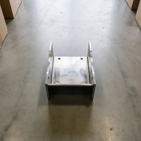Polished industrial metal bracket resting on a concrete warehouse floor with diffused lighting highlighting its finish