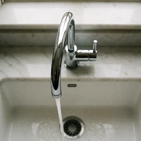 Modern kitchen sink with a shiny chrome faucet and flowing water on a polished white marble countertop