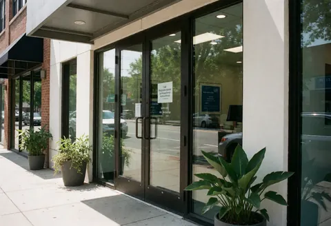 Exterior view of a computer support business entrance featuring glass doors, potted plants, and street reflections.