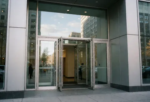 Clean and professional entrance to a modern corporate building featuring glass doors and city reflections.
