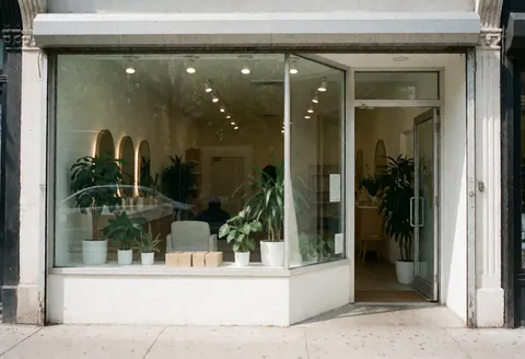 Exterior view of a hair salon featuring large windows, green plants, and an inviting entrance with a warm interior.