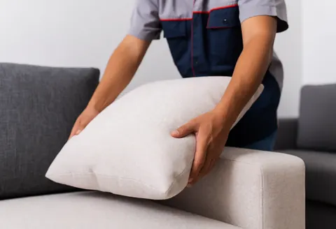 A man adjusts a cushion on a fabric sofa in a furniture store, demonstrating attentive customer service in a realistic setting.