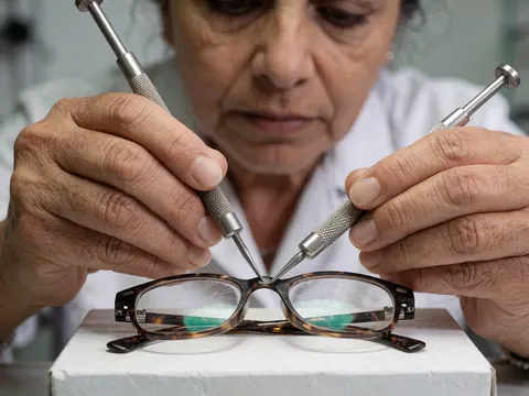 A technician uses metal tools to precisely adjust the screws on a glasses frame in a clean optical shop setting