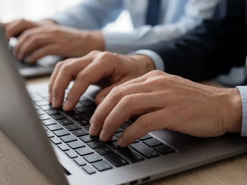 Close-up of a professional wearing a shirt and tie typing on a laptop in a modern office setting