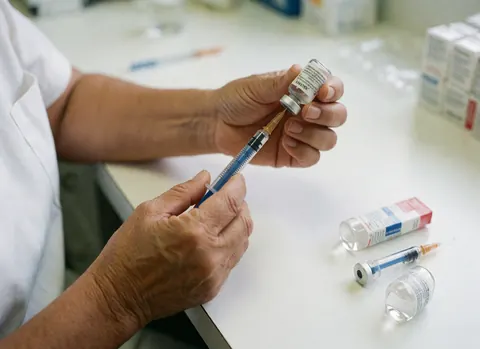 Close-up of older adult hands holding a syringe and medicine vial on a clean white clinical table
