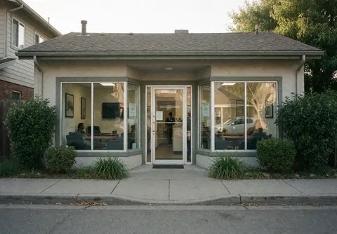 Exterior view of a driving school entrance featuring clean glass windows that reveal the interior seating and staff surrounded by pavement and greenery