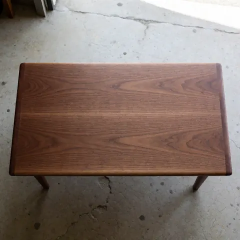 Solid wood table with polished finish, on cracked concrete floor.
