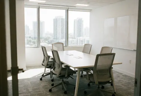 Spacious modern conference room featuring a white table, ergonomic chairs, and a large window with a panoramic city view.