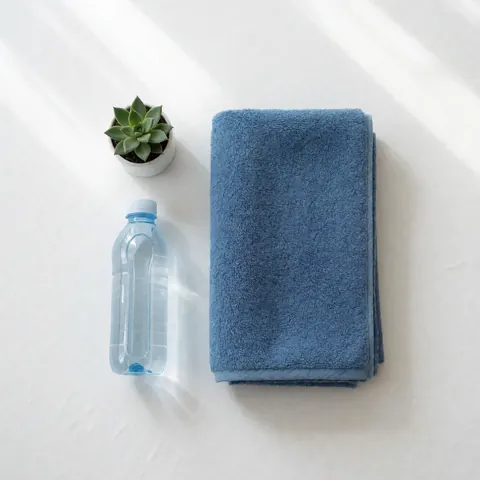 A folded blue towel, a water bottle, and a potted plant on a white surface.