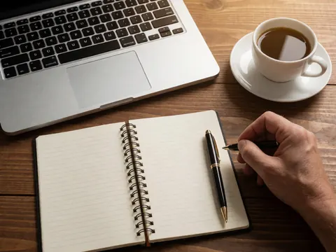 Wooden desk setup with open notebook, laptop, pen, and coffee cup for online courses or remote work