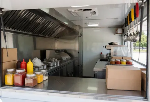 Clean modern food truck interior with stainless steel counter, condiments, hanging utensils, and kitchen equipment ready for service