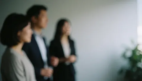Three business people in an office meeting, standing and talking, with a blurred background.