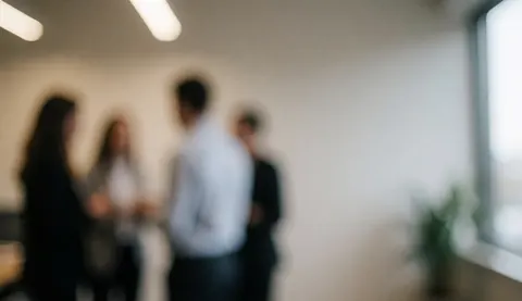 Blurry group of people in an office, talking near a window.