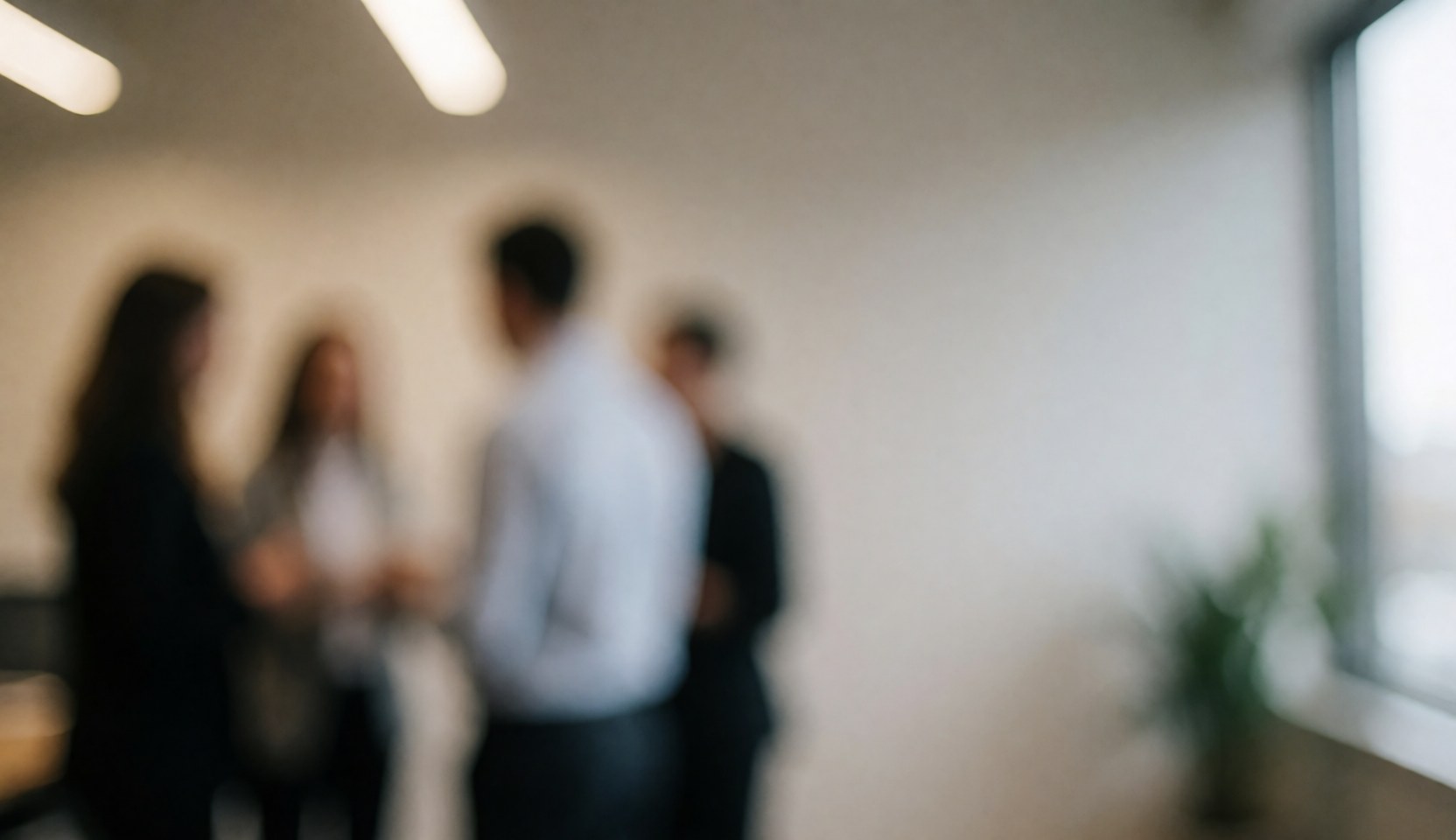 Blurry group of people in an office, talking near a window.