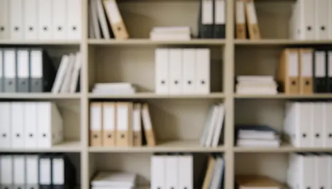 Office shelf with white, black, and brown binders organized on shelves.