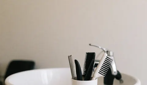Variety of brushes and combs for dogs in a dog grooming salon sink, with faucet and white basin.