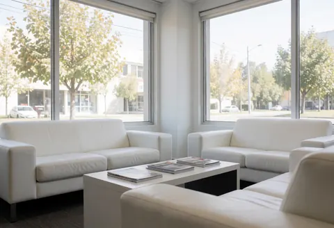 Modern waiting room with white sofas and coffee table, large windows overlooking the street.