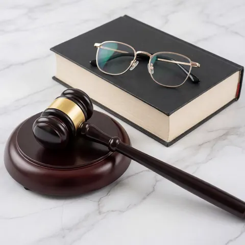 A judge's gavel, a book, and glasses rest on a white and gray marble surface.