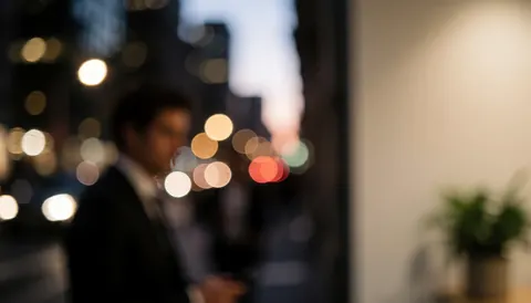 A businessman standing by a window with bokeh city lights at dusk.