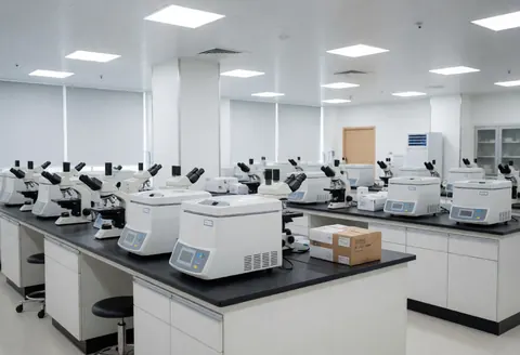 Clean empty clinical lab with microscopes and centrifuges on white and black tables under bright lighting