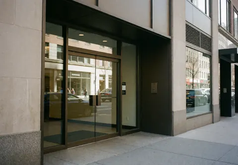 Modern office entrance with glass doors and stone walls, reflecting the street.