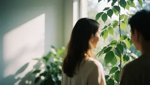 Two people from behind looking at green plants near a window with natural light.