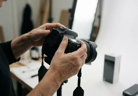 A person adjusts a DSLR camera with a large lens in a photography studio with white background and lighting equipment.