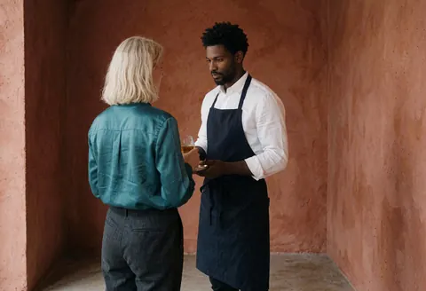 A bartender serves a drink to a customer in a bar with terracotta-colored walls.