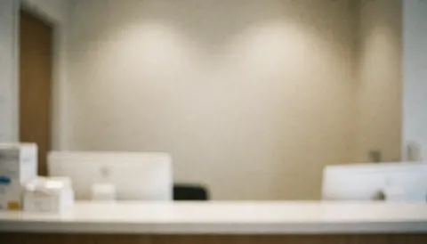 Blurry medical reception desk with computers and medicine boxes.
