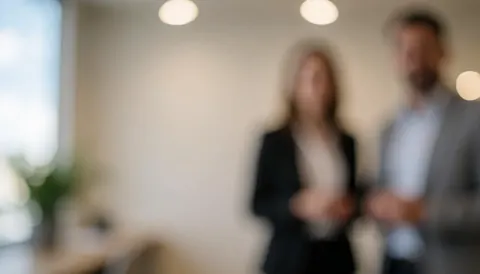 Two blurred business people in a modern office with bright lights and light walls.