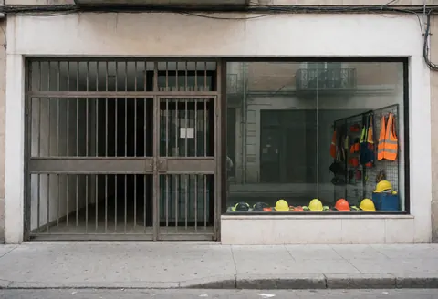 White storefront facade featuring a metal door and window displaying hard hats and safety vests on a clean sidewalk.