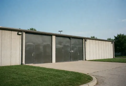 Industrial warehouse with large metal doors, concrete walls, and green grass around.