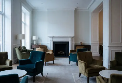 Hotel lobby with fireplace, armchairs, and round tables, calm and elegant atmosphere.