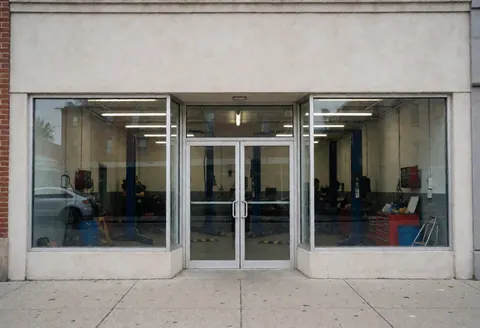 Exterior view of an auto repair business featuring large glass windows that reveal the interior workshop with tools and a raised vehicle.