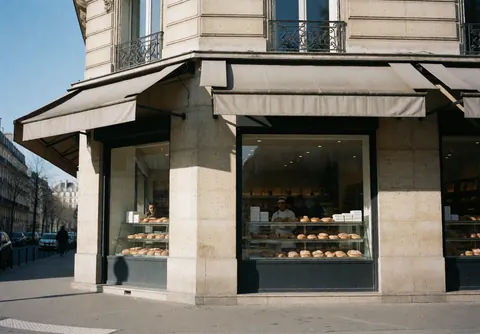 Pastry shop display case with pastries and bakers serving customers at a corner store.