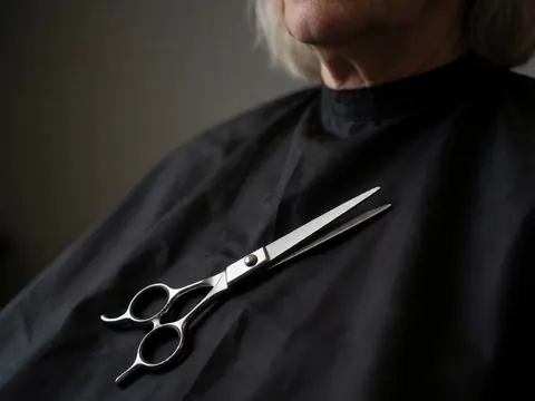 Close-up of professional hairdressing scissors resting on a black cape with dramatic lighting highlighting metallic details
